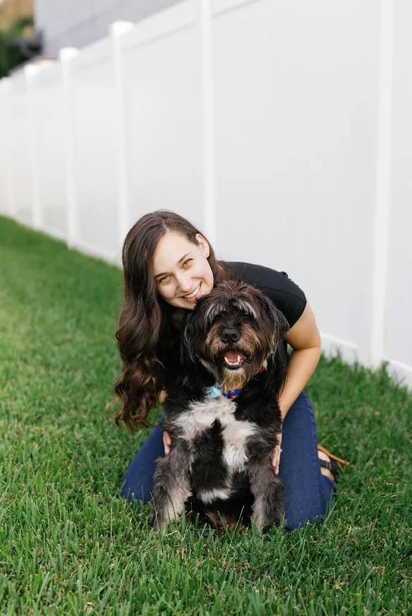 Dr. Carly Dworkin kneeling in front of a fence with her dog